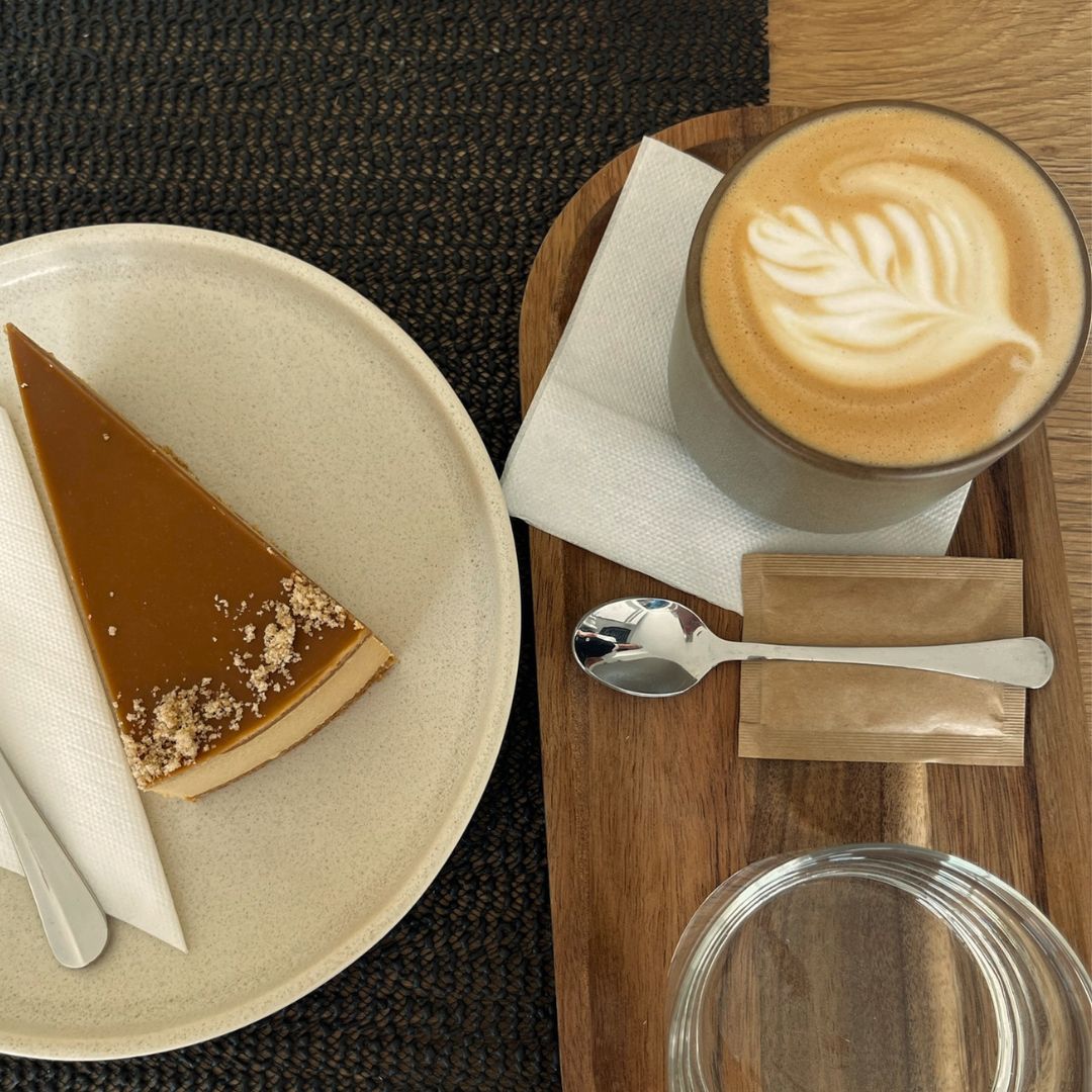 Šálek kávy s latte art a karamelový cheesecake na dřevěném prkénku
